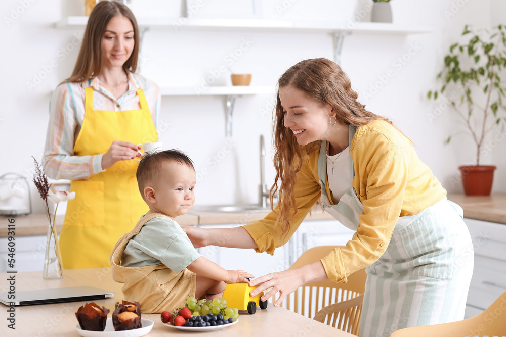 Young lesbian woman with her little baby in kitchen Young lesbian woman with her little baby in kitchen