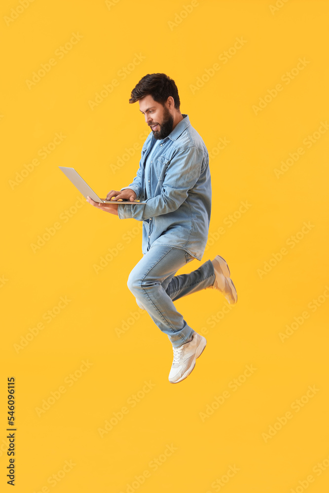 Handsome bearded man with laptop jumping on yellow background Handsome bearded man with laptop jumping on yellow background