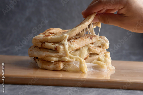 Hand picking a pupusa from a stack of pupusas on a wooden board and dark marble background photo