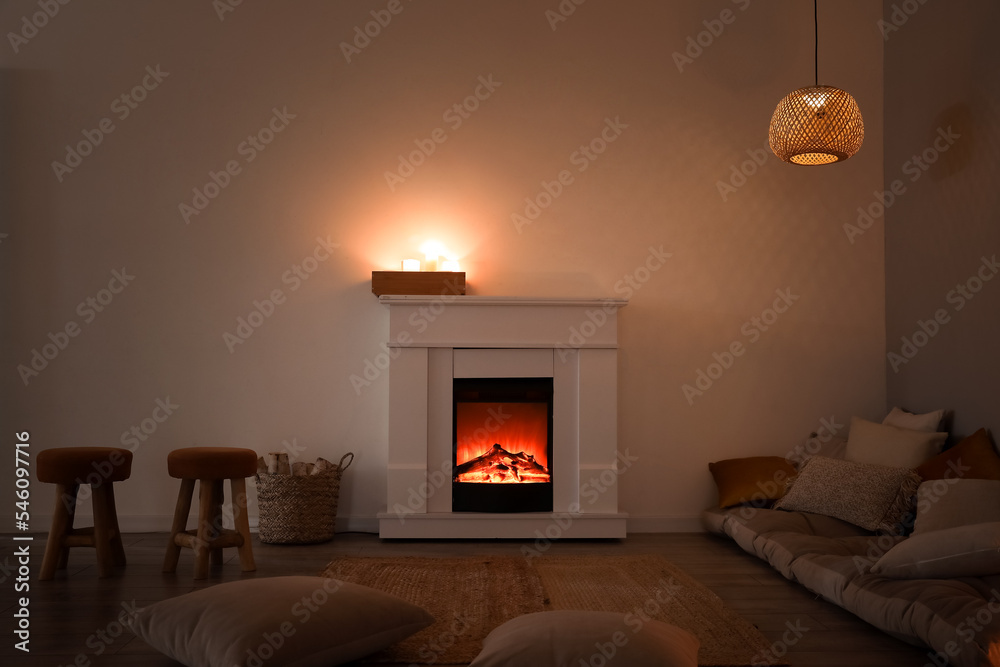 Fototapeta premium Interior of dark living room with fireplace, pillows and burning candles