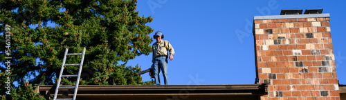 Senior man with gas powered leaf blower cleaning roof gutters on an apartment building, fall maintenance 
