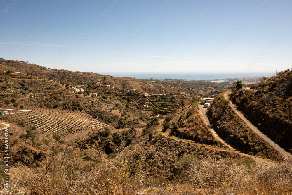The valley within this mountain range near Arenas in Andalusia has been modified by humans to accommodate roads on one side and irrigated farming fields on the other for hardy crops like almonds 