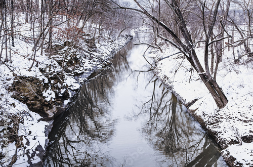 Midwestern creek after snowfall in winter; trees reflecting in water