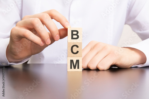 bcm, business continuity management text on cube blocks in businessman hands, man in white shirt