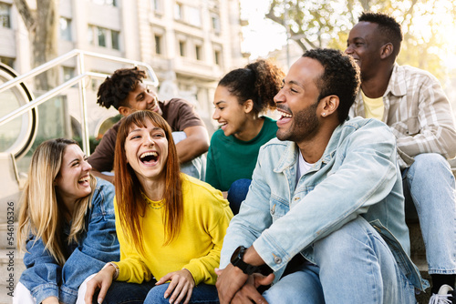 Young group of hispanic latin friends having fun together outdoors. Millennial multiracial people laughing while social gathering sitting on stairs at city street