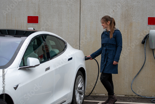 Happy pretty young smiling woman charges modern electric car