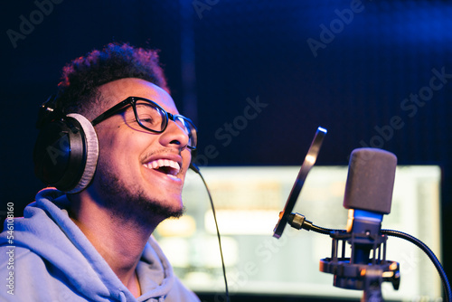 Male vocal artist, singer, podcaster with curly hair, headphones in sound studio recording new melody or album.