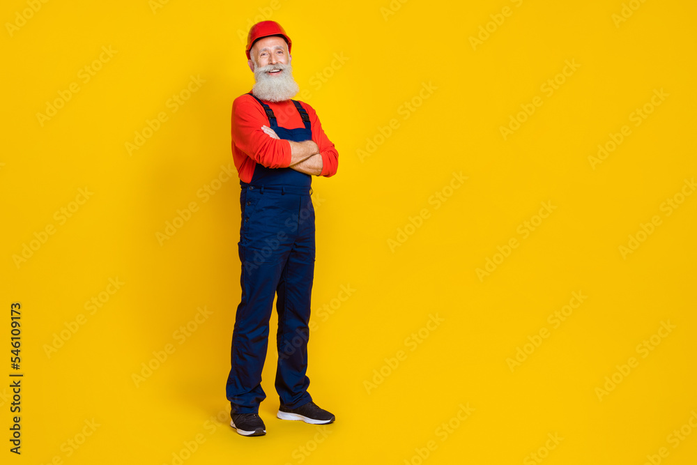 Full size photo of positive cheerful retired man builder with long beard red headgear hands crossed isolated on yellow color background Full size photo of positive cheerful retired man builder with long beard red headgear hands crossed isolated on yellow color background