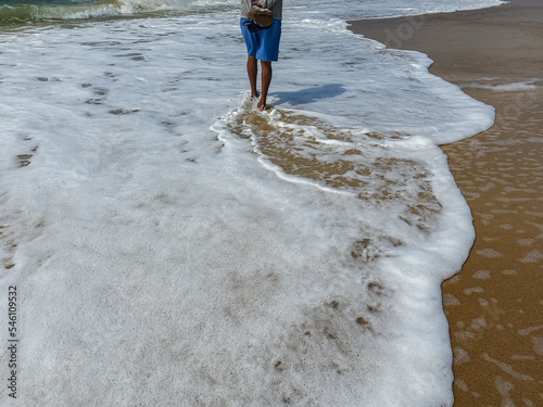 person walking on the beach with the waves full of foam photo