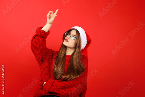 Attractive young woman in santa hat pointing fingers up, Christmas holidays.