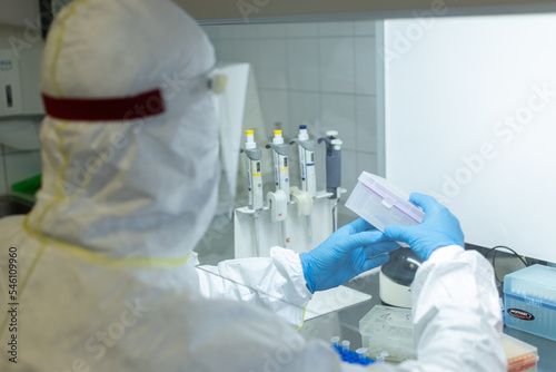 Naukowiec w laboratorium w kombinezonie bada próbki © Aleksandra