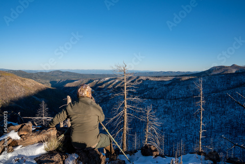 Hunter sits perched on the ridge in the mountains, using a spotting scope looking for elk. Taken in the Gila National Forest of New Mexico