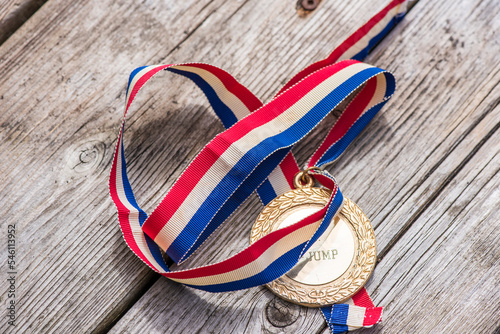 A gold medal with a red, white and blue ribbon on a wood surface.