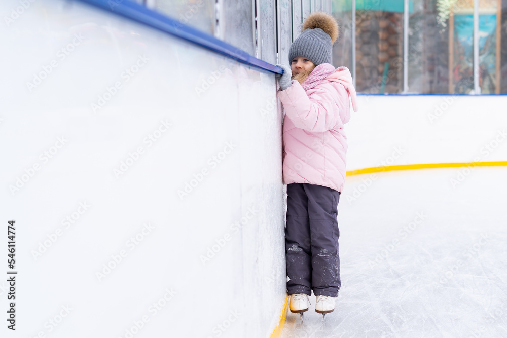 A little girl is skating on an ice rink, holding on to a support, a child is learning to skate, winter entertainment for children