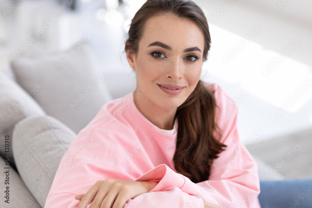 Portrait of a young woman in a pink sweatshirt on sofa in the living room, close-up.