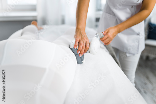 Lipomassage technique process. Unrecognizable caucasian beautician touching the leg area of her client covered with white non-invasive body suit. Professional equipment. High quality photo