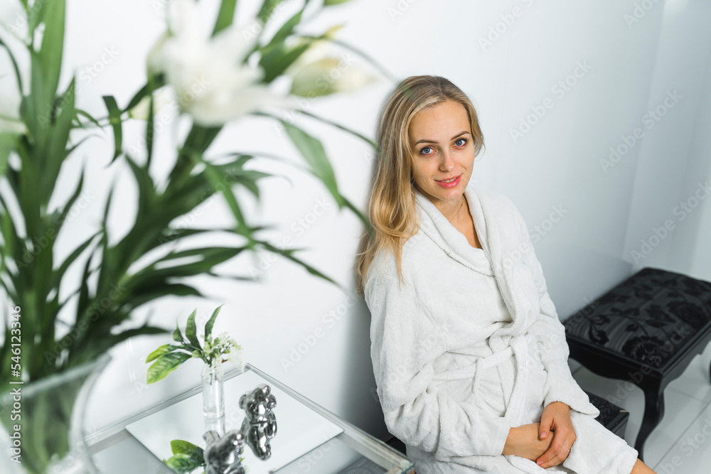 Relaxed excited adult caucasian blond-haired woman in white robe sitting and waiting for her facial treatment in her favorite beauty saloon. Looking at camera. High quality photo Relaxed excited adult caucasian blond-haired woman in white robe sitting and waiting for her facial treatment in her favorite beauty saloon. Looking at camera. High quality photo