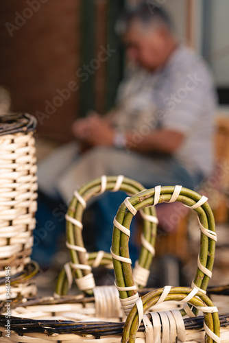 Wicker basket close up at workshop with old craftsman sitting at the back in blurred background. Selective focus