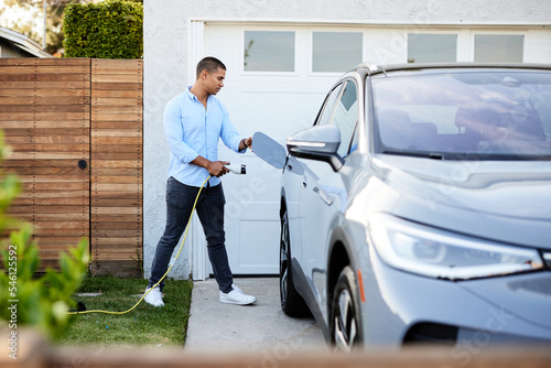 Full length of man with electric plug standing by car in back yard photo