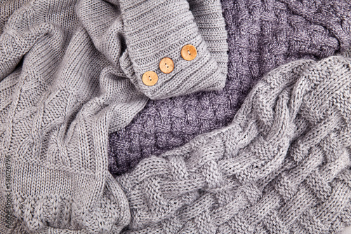 A pile of scattered gray knitted sweaters and scarves on the bed. View from above. Cozy autumn home background.