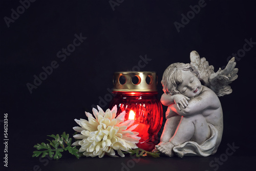 Funeral candle, flower and angel figurine on black background