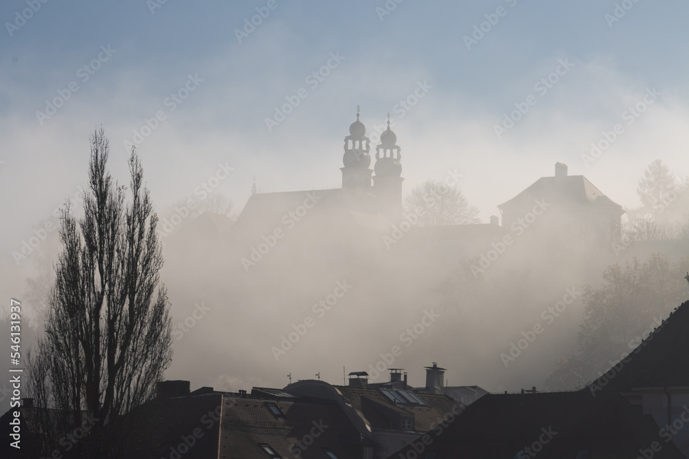 Seventeenth-century church in thick fog seen over the roofs of houses in Passau, Germany