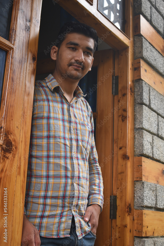 Indian guy standing at the wooden polished door and looking away Indian guy standing at the wooden polished door and looking away