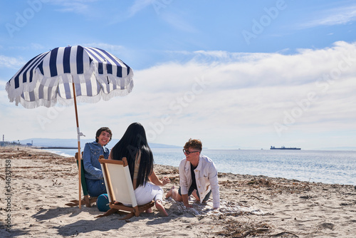 friends at beach by umbrella and beach chairs