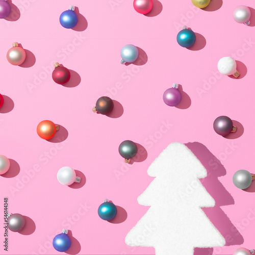 Trendy Christmas pattern made with colorful baubles decoration and christmas tree on pink background with the sharp shadows of the winter sun. Minimal Concept New Year's and Christmas atmosphere.