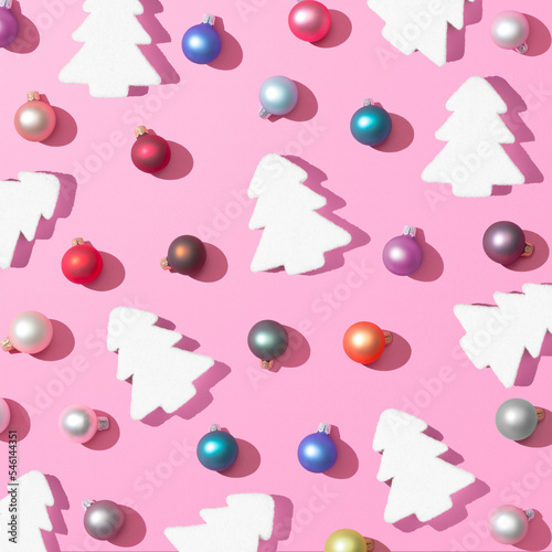 Trendy Christmas pattern made with colorful baubles decoration and christmas tree on pink background with the sharp shadows of the winter sun. Minimal Concept New Year's and Christmas atmosphere.