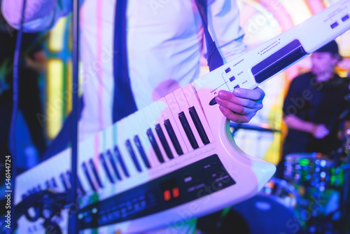 Concert view of a keytar synthesizer player with vocalist and musical jazz rock band orchestra performing in a background, electronic keyboard instrument guitar performer on a stage photo