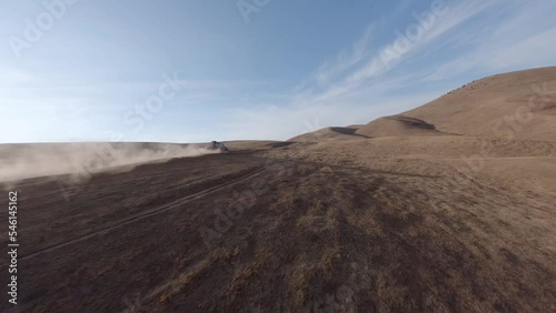 SUV car speed race riding on dirt road at desert sand mountain landscape with blue sky aerial view. FPV sports drone shot extreme dust automobile drive journey transportation offroad rally tourism 4k