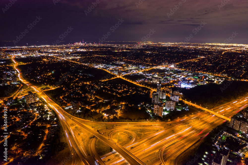 Fototapeta premium Top view of car traffic at intersection lane and buildings. Long exposure of urban cityscape at night. Modern city in Canada full of night lights from energy and power.