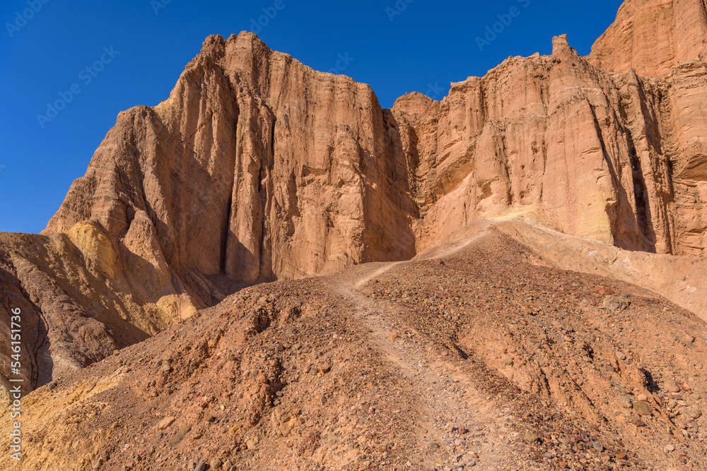 Red Cathedral - A rocky trail winding towards steep cliffs of Red Cathedral, Death Valley National Park, California, USA.