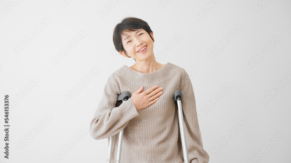 安堵の表情をする松葉杖をついたミドル女性 医療保険イメージ 安堵の表情をする松葉杖をついたミドル女性 医療保険イメージ
