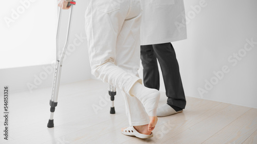 医者に介助されながら松葉杖をついて歩くミドル女性　リハビリイメージ