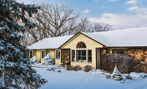 View of traditional suburban Midwestern house and front yard in winter after snowstorm; blue sky with clouds in background