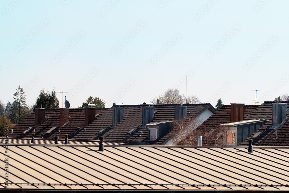 Top view of the roof of townhouses against the blue sky. Tiled Bavarian roofs with chimneys and skylights. Brick and metal air ducts or chimneys.