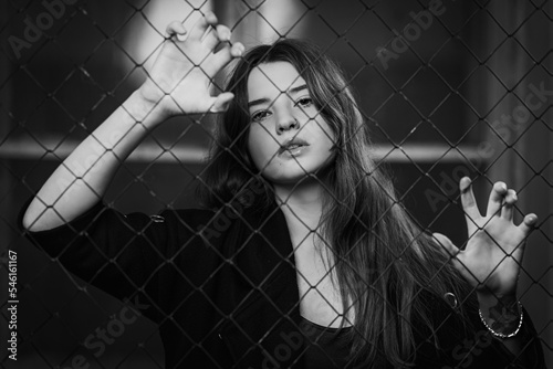 portrait Young dark-haired woman who stands behind a mesh fence in the distance. The concept of a lonely and sad woman