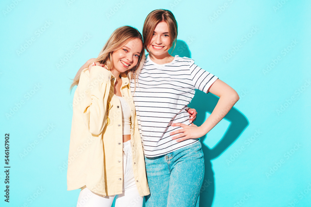 Two young beautiful smiling brunette hipster female in trendy summer clothes. Sexy carefree women posing near blue wall. Positive models having fun. Cheerful and happy Two young beautiful smiling brunette hipster female in trendy summer clothes. Sexy carefree women posing near blue wall. Positive models having fun. Cheerful and happy