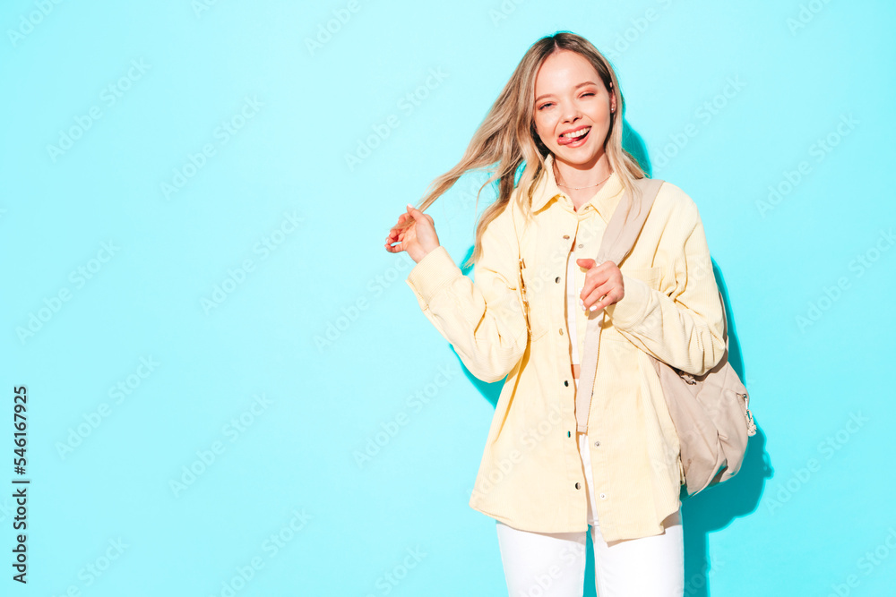 Young beautiful woman looking at camera.Trendy female smiling in casual summer clothes. Positive and funny model posing on grey background in studio with backpack Young beautiful woman looking at camera.Trendy female smiling in casual summer clothes. Positive and funny model posing on grey background in studio with backpack