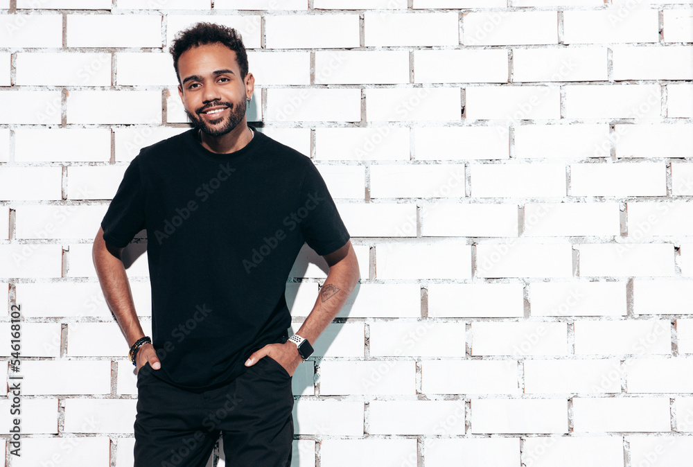 Handsome smiling hipster model. Sexy unshaven man dressed in summer t-shirt and jeans clothes. Fashion male posing near white brick wall in studio at sunny day. Isolated Handsome smiling hipster model. Sexy unshaven man dressed in summer t-shirt and jeans clothes. Fashion male posing near white brick wall in studio at sunny day. Isolated