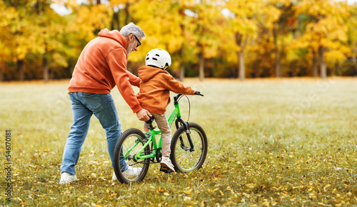 Fotografia Happy family grandfather teaches child grandson  to ride a bike in park