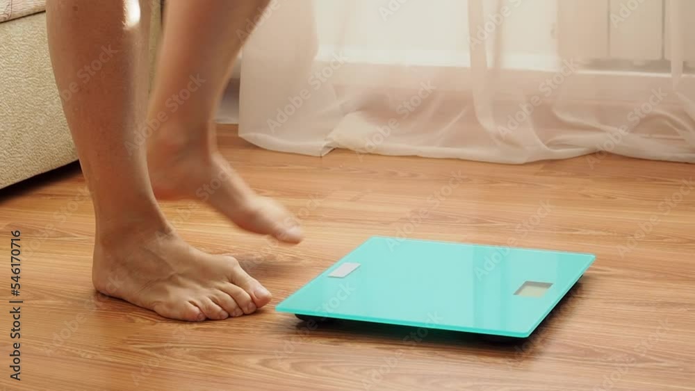 Senior woman gets up from the sofa in the morning, stands on the scales with bare feet, rejoices in weight loss Senior woman gets up from the sofa in the morning, stands on the scales with bare feet, rejoices in weight loss
