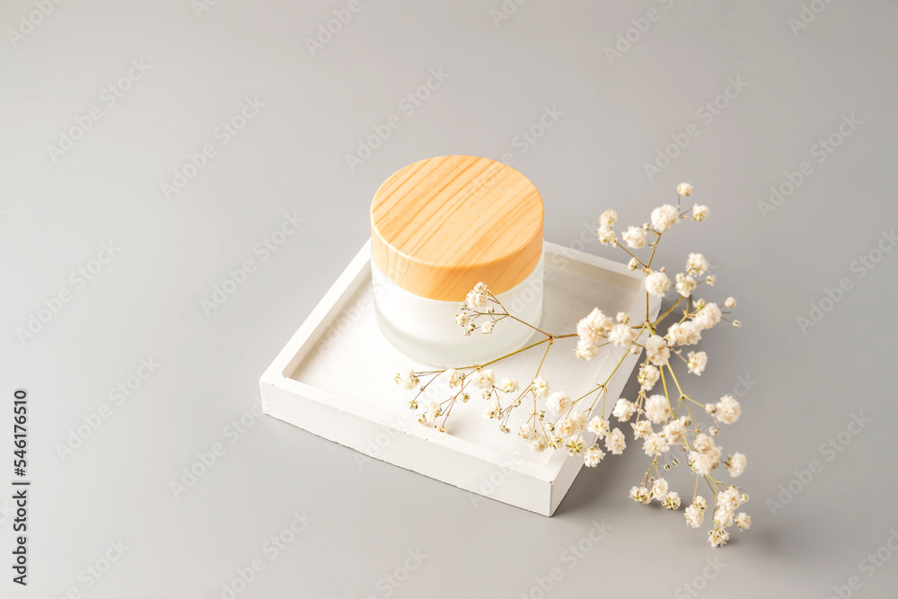 Moisturizer cream in frosted glass jar and dry white flowers on beige background, close-up. Care for sensitive skin with natural extract. Summer or autumn skincare body care concept