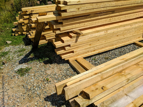 Wooden boards stacked in rows and lie on the ground. Boards for construction are sawn with bars. Close-up