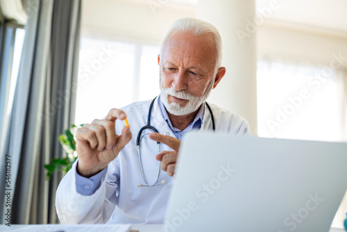 Doctor online. Senior medic talking to client on laptop computer from his office. Mature male therapist explaining medical treatment to patient through a video call with laptop in the consultation.