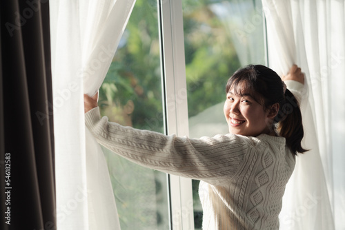 Happy woman opening window curtains in the morning.
