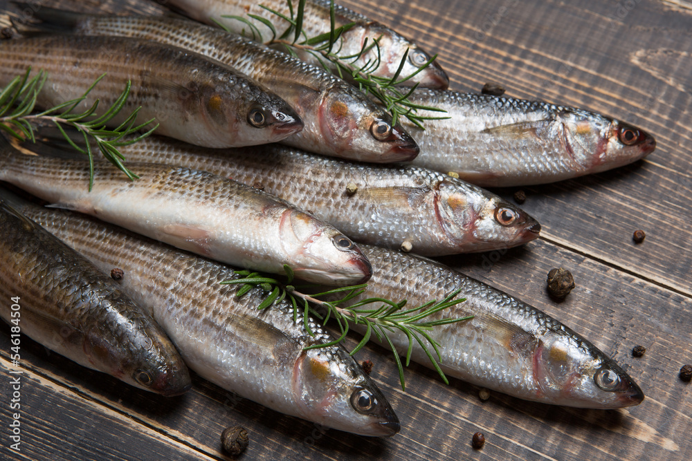 Heap of silver mullet, spices and green sprigs of rosemary, on old boards, rustic style Heap of silver mullet, spices and green sprigs of rosemary, on old boards, rustic style