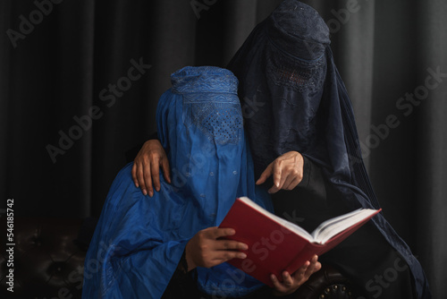 Afghan Muslim women with burka traditional costume, reading holy  Quran against the dark background photo